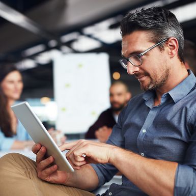 A man with glasses using a tablet in an office environment.