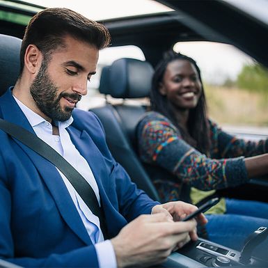 Businessman uses an app in a car while a woman drives